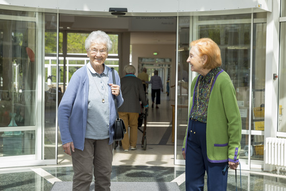 Zwei Seniorinnen stehen lächelnd am Eingang der Residenz, was ist los in der Residenz am Wiesenkamp, Veranstaltungskalender, Kulturveranstaltungen für Senioren und Seniorinnen, Hamburg-Volksdorf