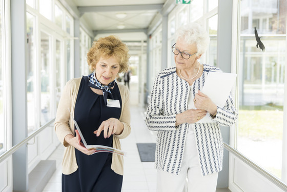 Eine Residenzmitarbeiterin berät eine interessierte Seniorin, Außenansicht, Residenzberatung Eine Residenzmitarbeiterin berät eine interessierte Seniorin, Außenansicht, Residenzberatung