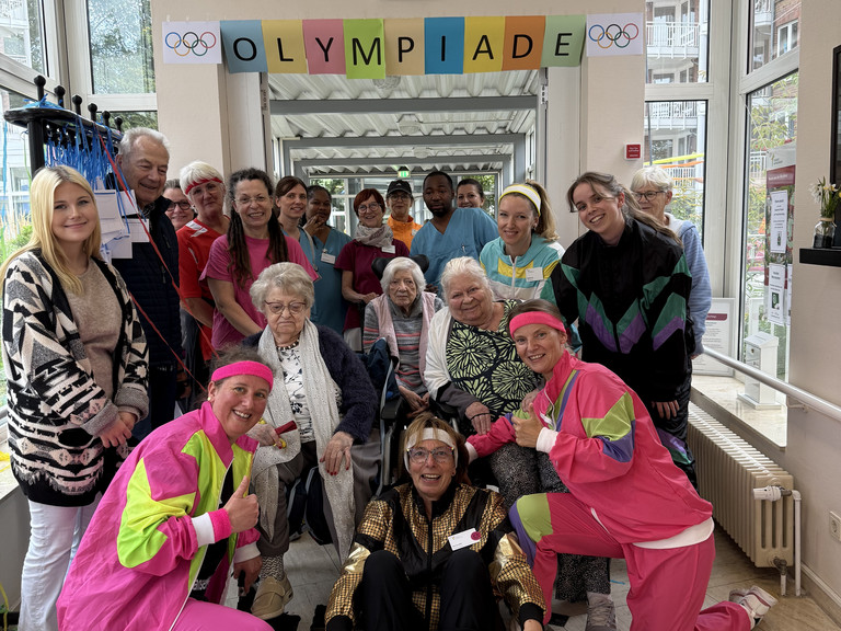 Mehrere Bewohnende und Angestellte der Residenz am Wiesenkamp in Hamburg Volksdorf posieren in bunter Sportkleidung im Rahmen der Bewohner Olympiade Mehrere Bewohnende und Angestellte der Residenz am Wiesenkamp in Hamburg Volksdorf posieren in bunter Sportkleidung im Rahmen der Bewohner Olympiade